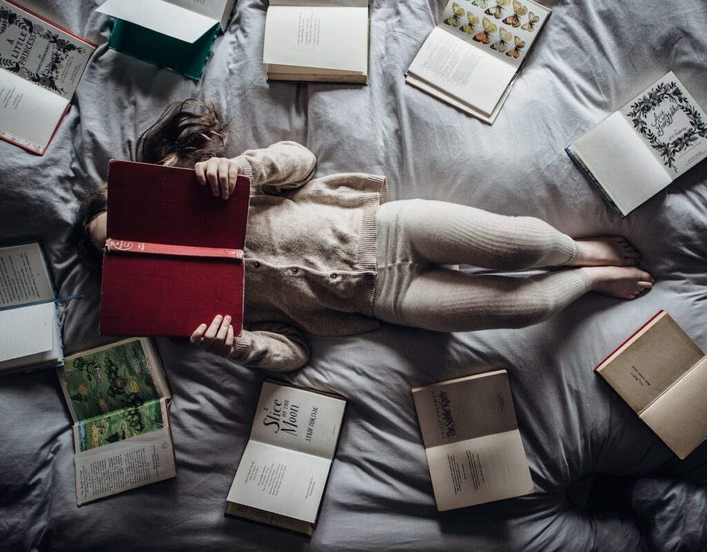 a little girl laying on a bed with lots of books - book journal