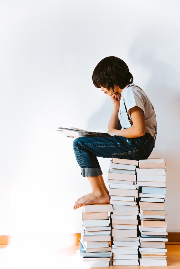 kid sitting on a pile of books reading - book journal