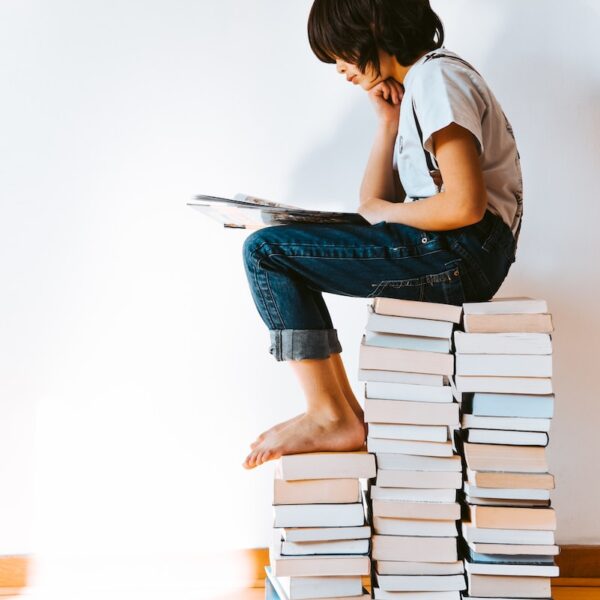 kid sitting on a pile of books reading - book journal