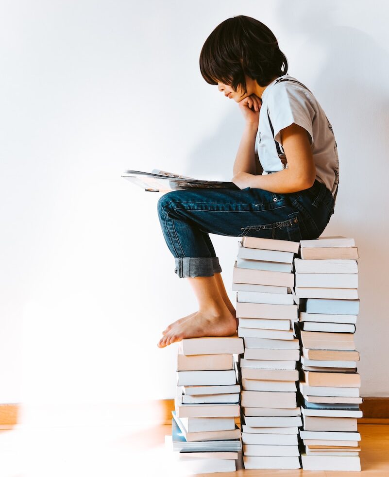 kid sitting on a pile of books reading - book journal